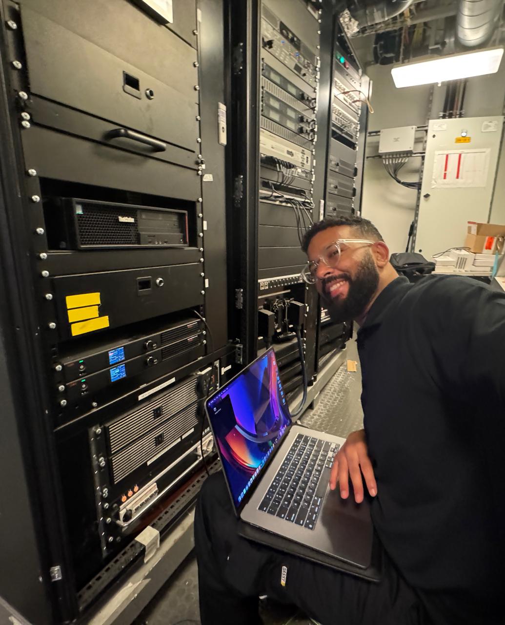 Working on a laptop beside the broadcast equipment racks
